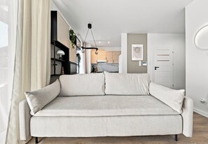 A neutral-toned sofa in a modern living room with a minimalist design, a visible kitchen area, and a door leading to another room. - Rymanowska Chic Apartment (Rzeszów)