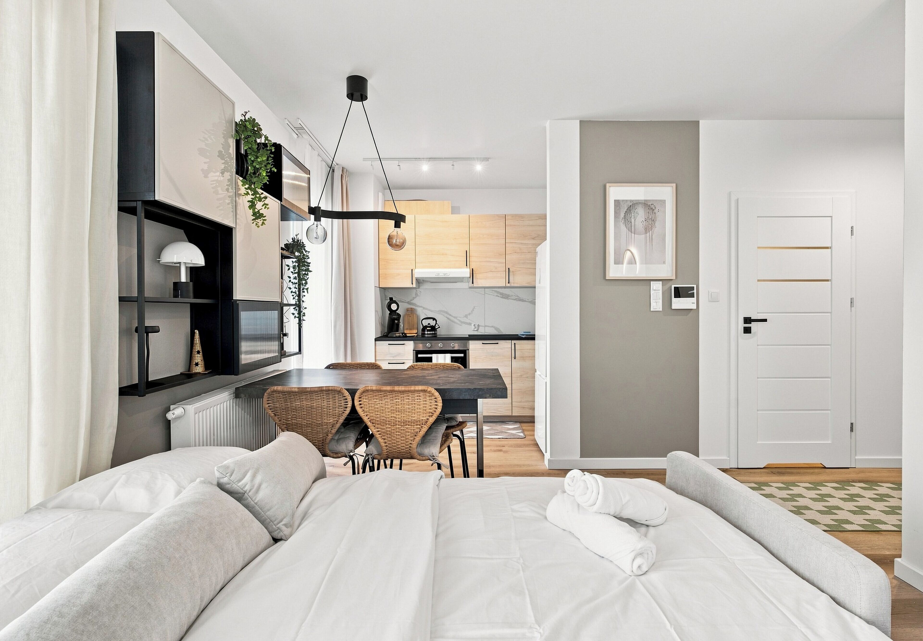 A modern hotel room with a bed, a dining table with chairs, a kitchen area, and a bathroom.