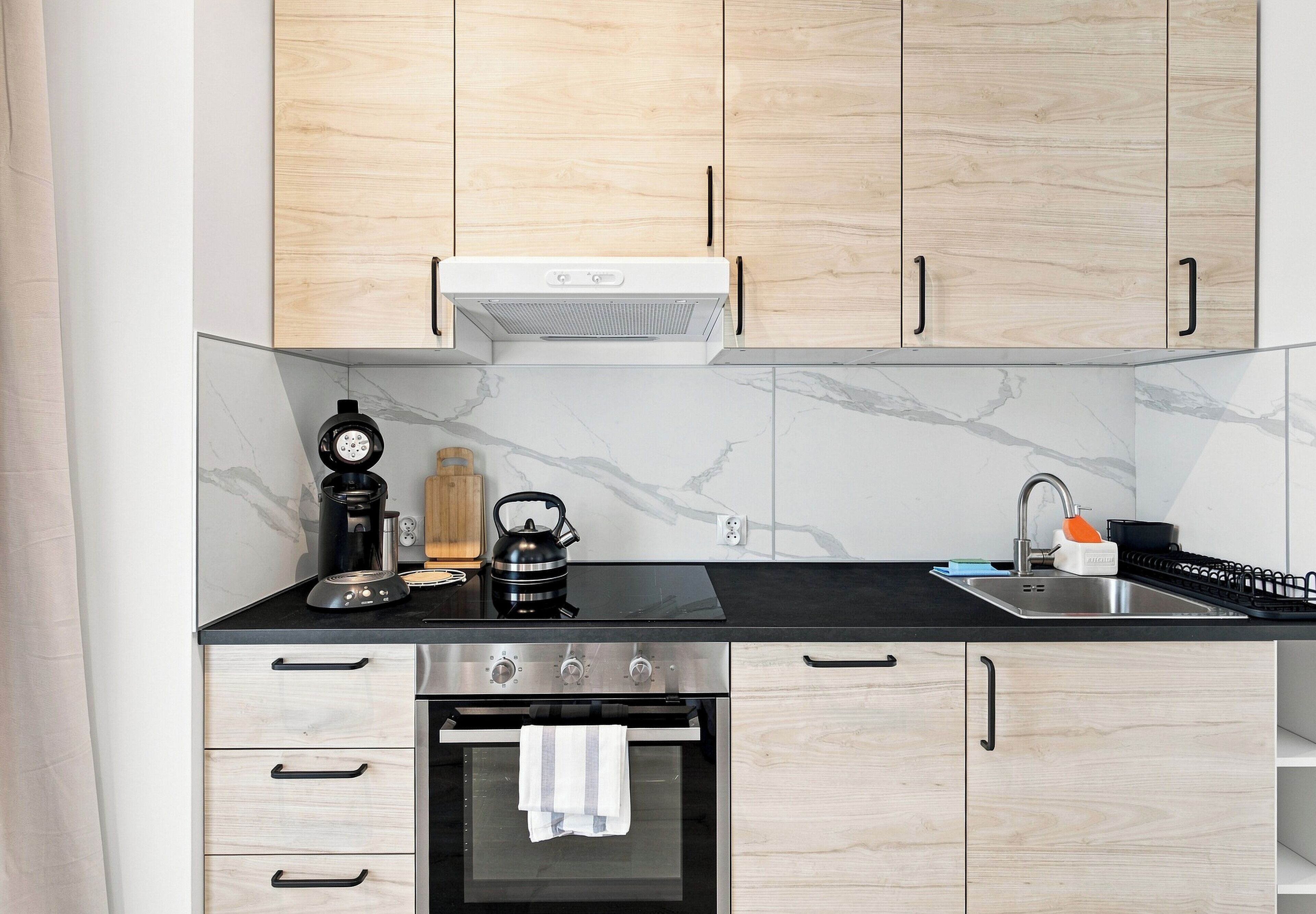 Een moderne keuken met houten kastjes, een zwart aanrecht, een roestvrijstalen oven en een koffiezetapparaat.