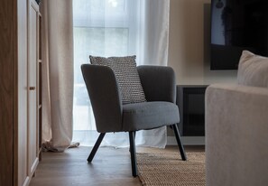 A modern living room with a grey armchair, a patterned cushion, and a television mounted on the wall. - Rymanowska Chic Apartment (Rzeszów)