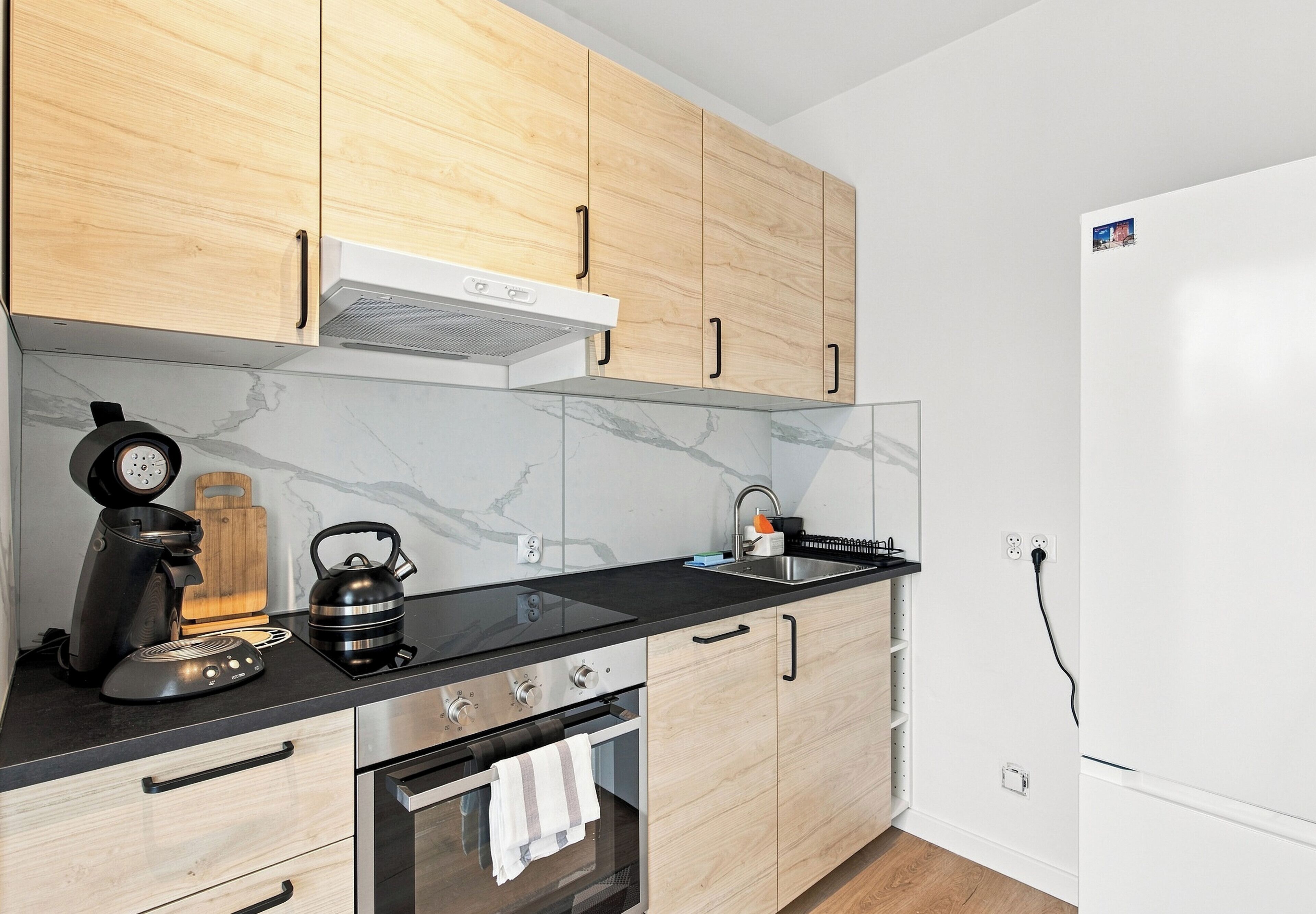 Eine moderne Küche mit Holzschränken, einer schwarzen Arbeitsplatte, einem eingebauten Backofen und einem weißen Kühlschrank.