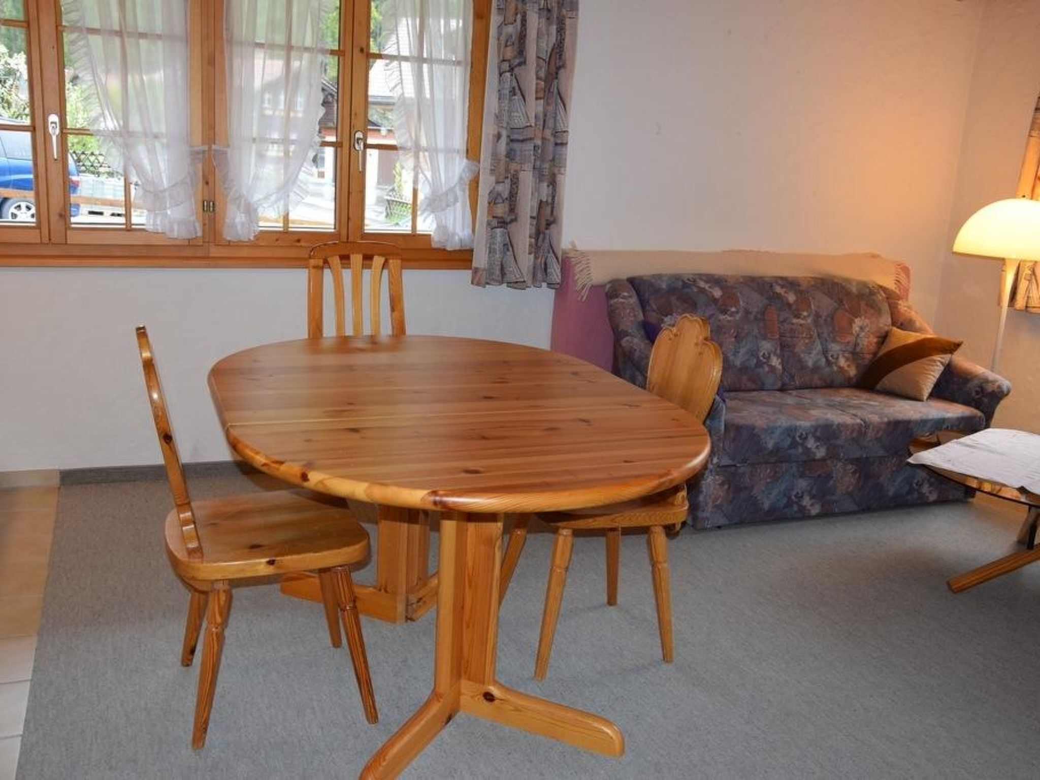 A dining area with a wooden table and chairs, a sofa, and a lamp.