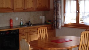 A kitchen with wooden cabinets, a dining table with chairs, a red cutting board, and a window with curtains. - Favre OG Ost Appartement/Fewo, Dusche oder Bad, WC, 1 Schlafraum 2-Bett-Wohnung by Interhome (Matten  (St. Stephan))