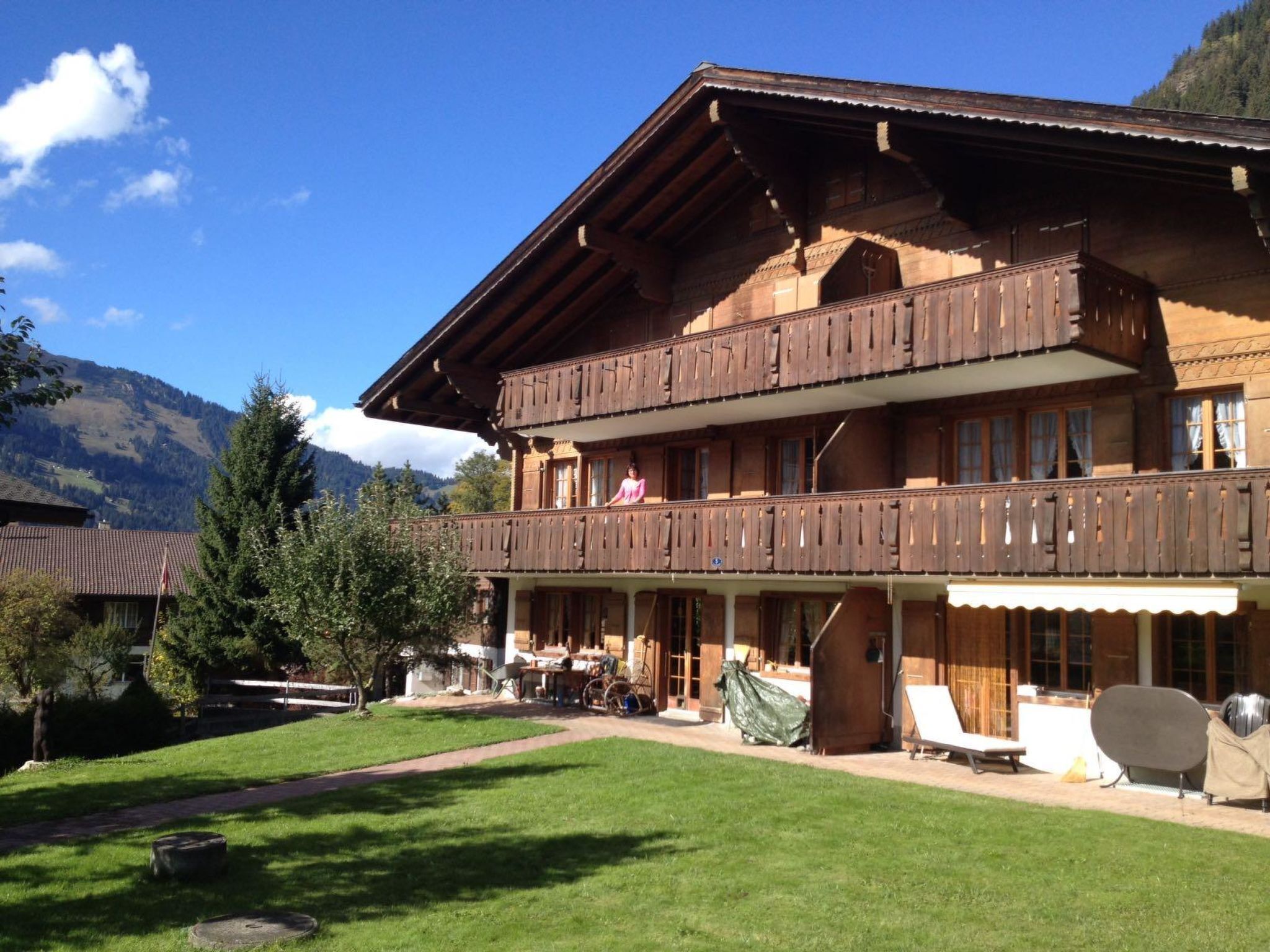A two-story wooden chalet with a balcony, a covered patio area with outdoor furniture, and a mountainous backdrop.
