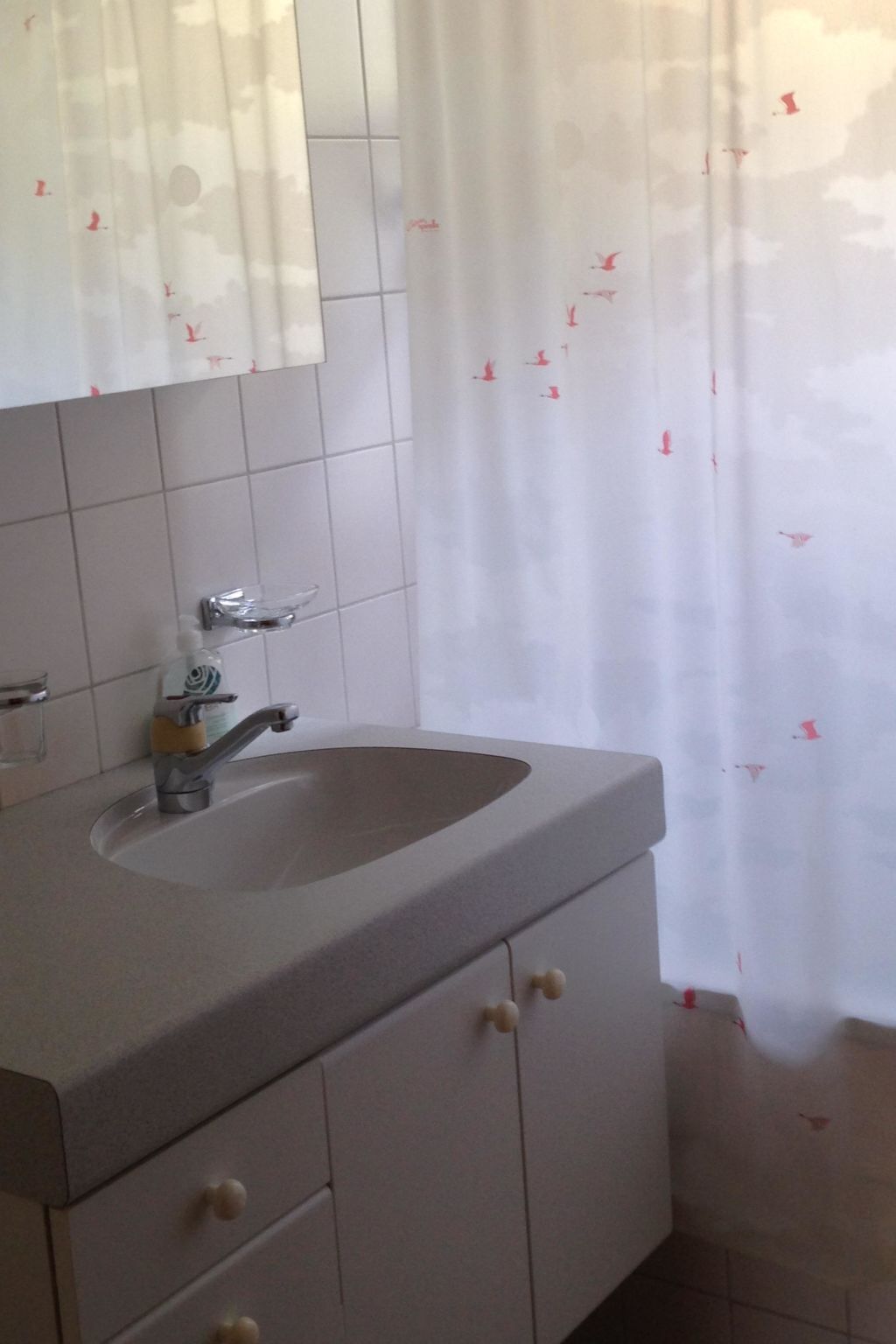 Et badeværelse med håndvask, spejl og flisebeklædte vægge.