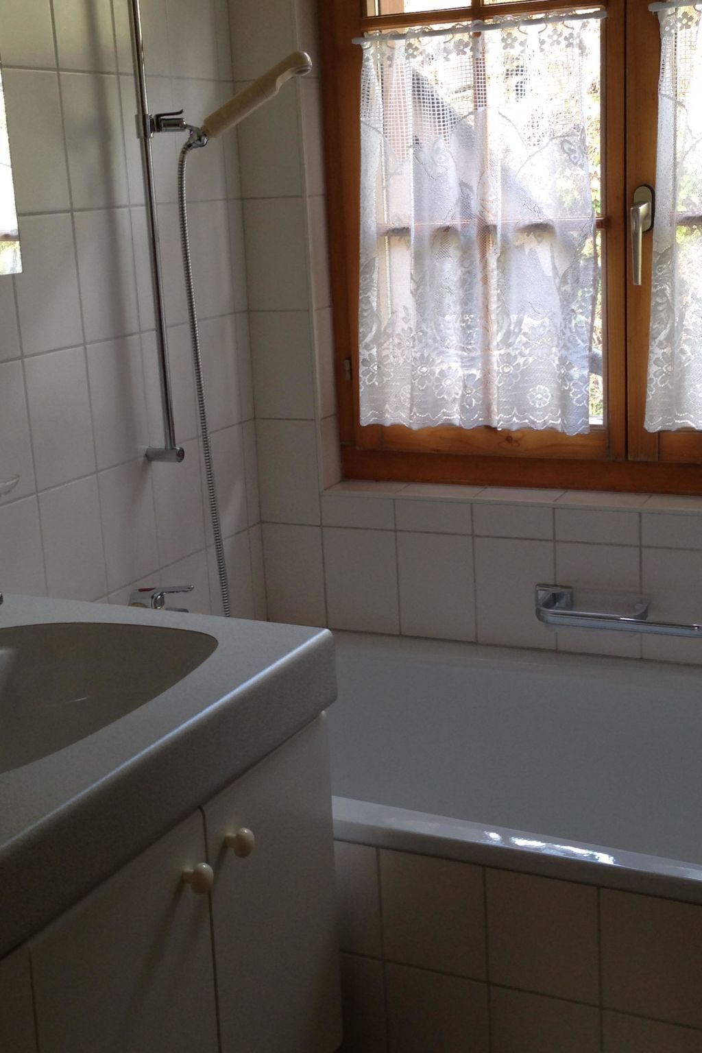 A bathroom with a bathtub, a shower, and a window with lace curtains.