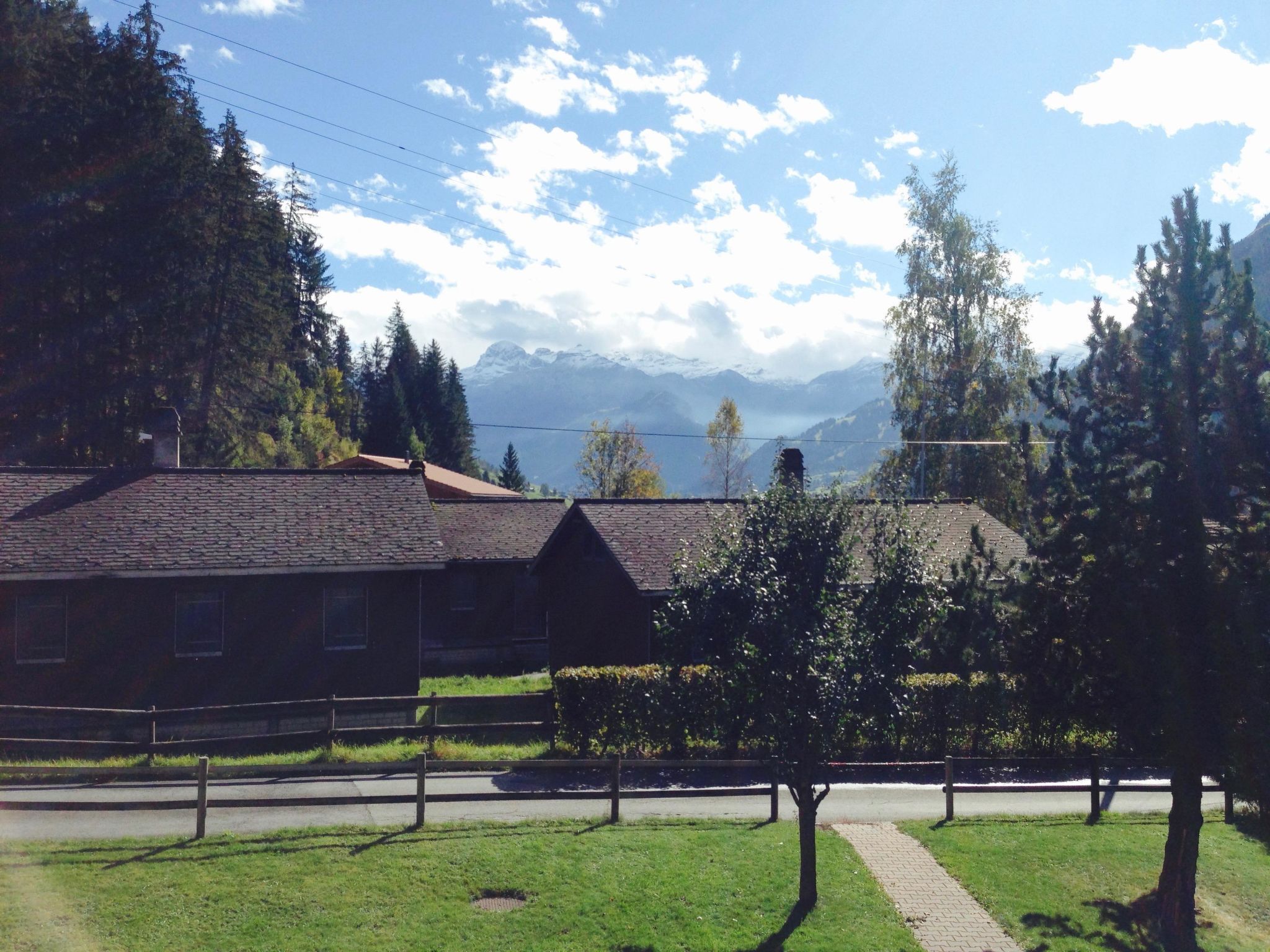 A traditional chalet with a sloped roof, surrounded by a well-maintained lawn and a wooden fence.