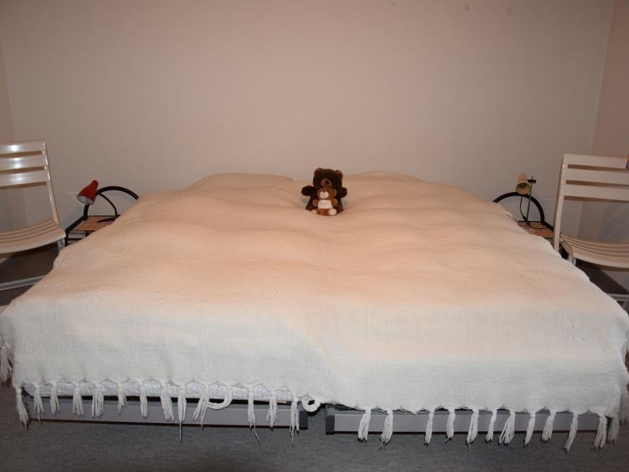A bed with a white blanket and a teddy bear in the center.