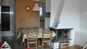 A dining area with a table set for four, a fireplace, and a kitchen visible in the background. - Chutzli Appartement/Fewo, Dusche oder Bad, WC, 2 Schlafräume 4-Bett-Wohnung by Interhome (Matten  (St. Stephan))