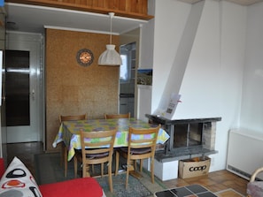 Ein Essbereich mit Tisch für vier Personen, einem Kamin und einer sichtbaren Küche im Hintergrund.