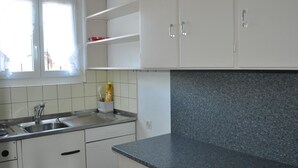 A kitchen with white cabinets, a granite countertop, a stainless steel sink, and a window with curtains. - Chutzli Appartement/Fewo, Dusche oder Bad, WC, 2 Schlafräume 4-Bett-Wohnung by Interhome (Matten  (St. Stephan))