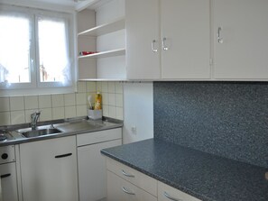 Eine Küche mit weißen Schränken, einer Arbeitsplatte aus Granit, einer Spüle aus Edelstahl und einem Fenster mit Vorhängen.