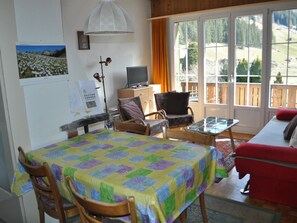 Ein gemütliches Zimmer mit einem Bett, einem Fernseher, einem Schreibtisch und einem Sessel. Ein Fenster bietet Blick ins Freie.