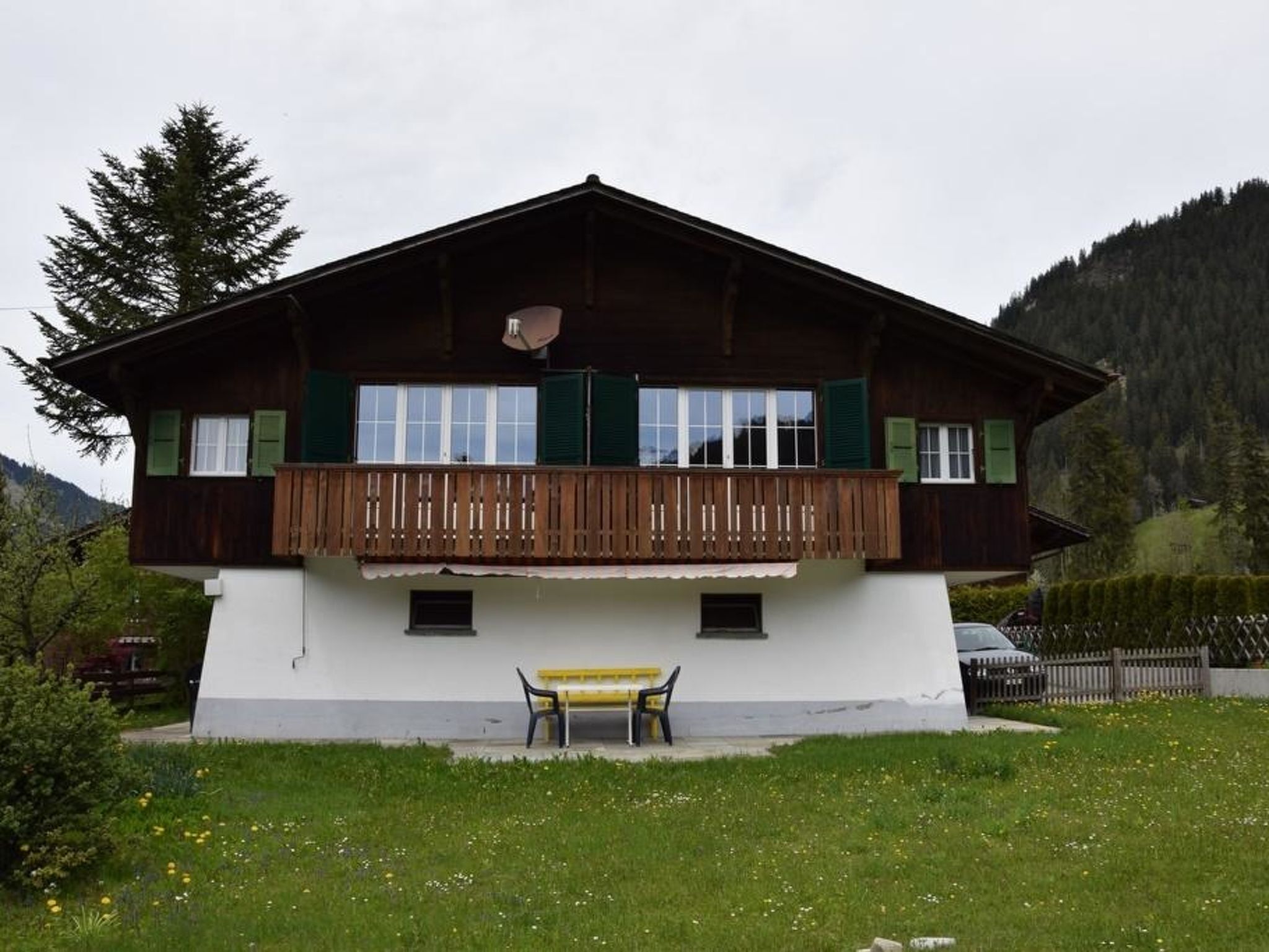 Eine zweistöckige Holzchalet mit Balkon und einer Bank vor der Fassade, vor einer Bergkulisse.