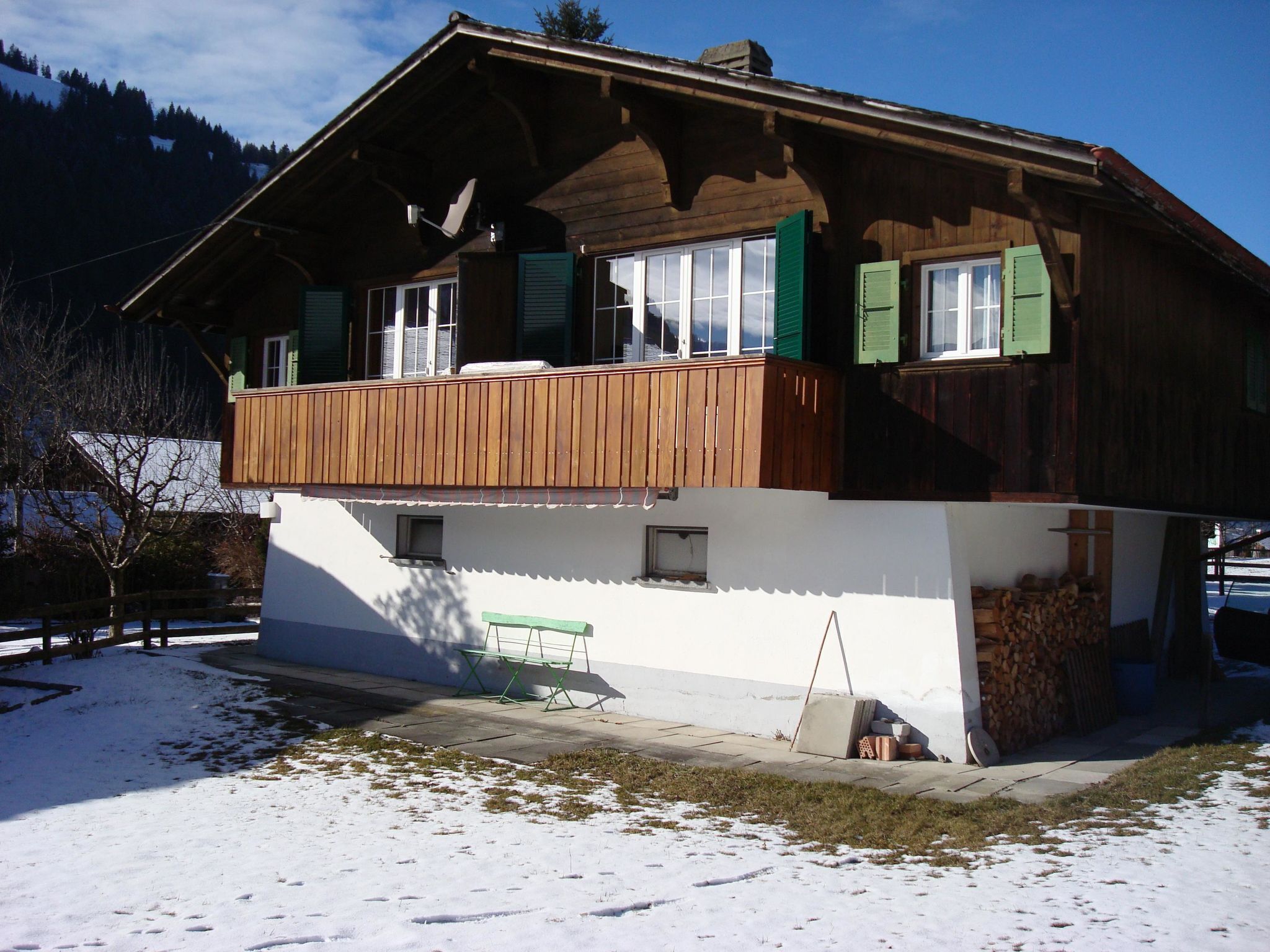 Une maison en bois à deux étages, dotée d’un balcon, d’une petite remise attenante et d’un banc à l’extérieur.