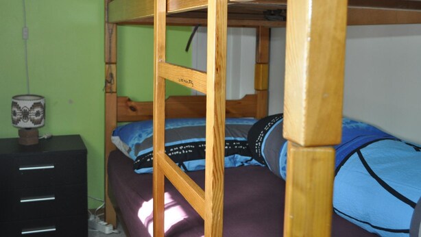 A bunk bed with a wooden frame, a bedside table with a lamp, and a wall socket. - Chutzli Appartement/Fewo, Dusche oder Bad, WC, 2 Schlafräume 4-Bett-Wohnung by Interhome (Matten  (St. Stephan))