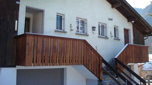 A building with a wooden staircase leading to a landing, a nameplate on the wall, and a garage door. - Chutzli Appartement/Fewo, Dusche oder Bad, WC, 2 Schlafräume 4-Bett-Wohnung by Interhome (Matten  (St. Stephan))