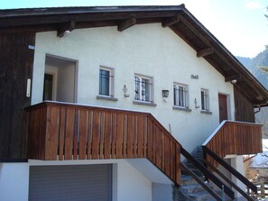 Ein Gebäude mit einer Holztreppe, die zu einer Zwischenplattform führt, einem Namensschild an der Wand und einer Garagentür.
