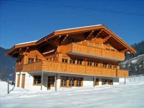 Ein mehrstöckiges Holzhaus mit Balkonen vor einer verschneiten Landschaft.