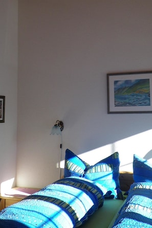 Ein Zimmer mit einem Bett, Kissen, einer Wandlampe und einem gerahmten Bild.