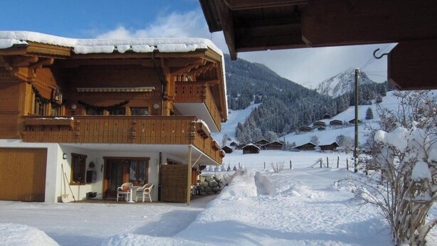 A wooden chalet with a balcony, a covered outdoor seating area, and a view of snow-covered mountains. - Morgenstern Appartement/Fewo, Dusche, WC, 1 Schlafraum 4-Bett-Wohnung by Interhome (St Stephan)