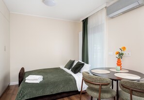 A hotel room with a bed, a dining table with chairs, a vase with flowers, and an air conditioning unit. - Rondo Matecznego Signature Studio (Kraków)