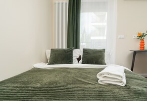 A neatly made bed with green bedding, a white pillow, and a folded white towel. - Rondo Matecznego Signature Studio (Kraków)