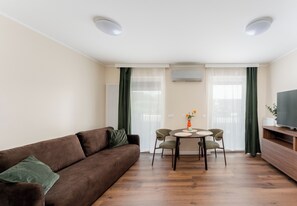 Ein Wohnzimmer mit braunem Sofa, einem Esstisch mit Stühlen, einem Fernseher auf einem Holzschrank und einer Heizung.