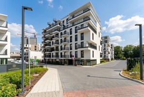 Ein modernes Mehrfamilienhaus mit mehreren Balkonen, einem Parkplatz und blauem Himmel.