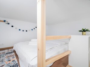 Quarto minimalista com uma cama de solteiro e beliche, uma guirlanda de bolas decorativas na parede e uma planta em vaso sobre uma mesa de cabeceira.