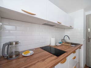 Een moderne keuken met witte metrobetegels, een houten aanrechtblad, een waterkoker, een weegschaal en een zwart inductiekookveld.