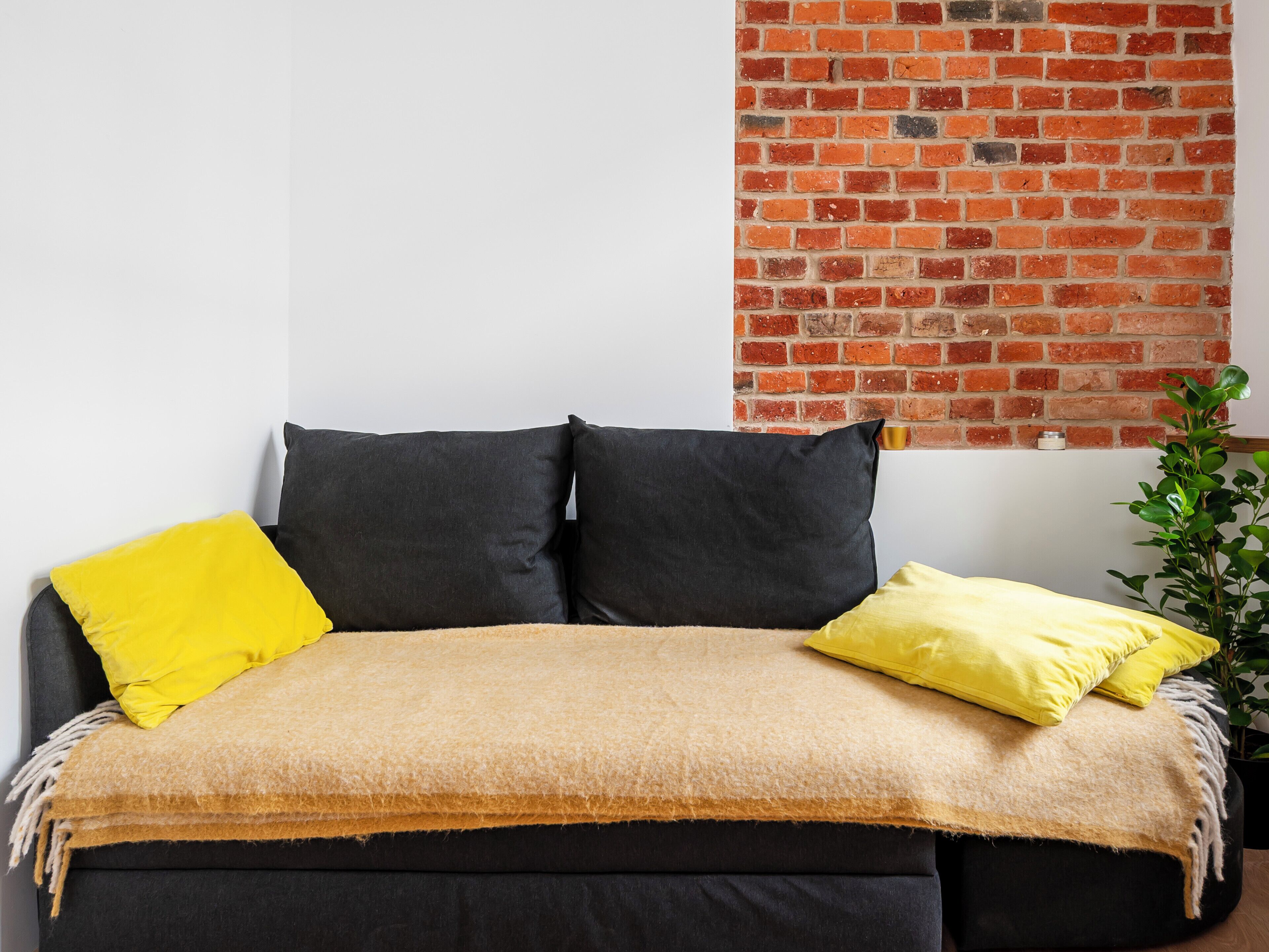A bed with a dark headboard, a beige blanket, and two pillows in yellow and gray.