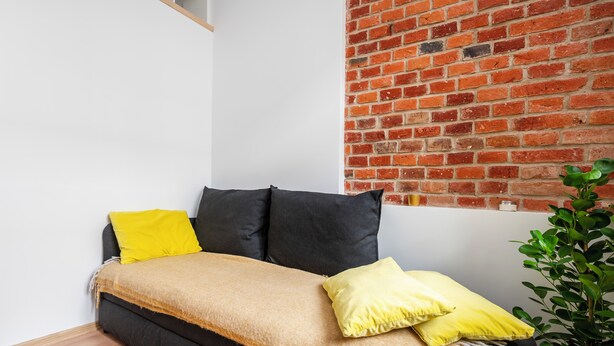 Ein Bett mit schwarzem Gestell, einem gelben Kissen und einer beige farbenen Decke.