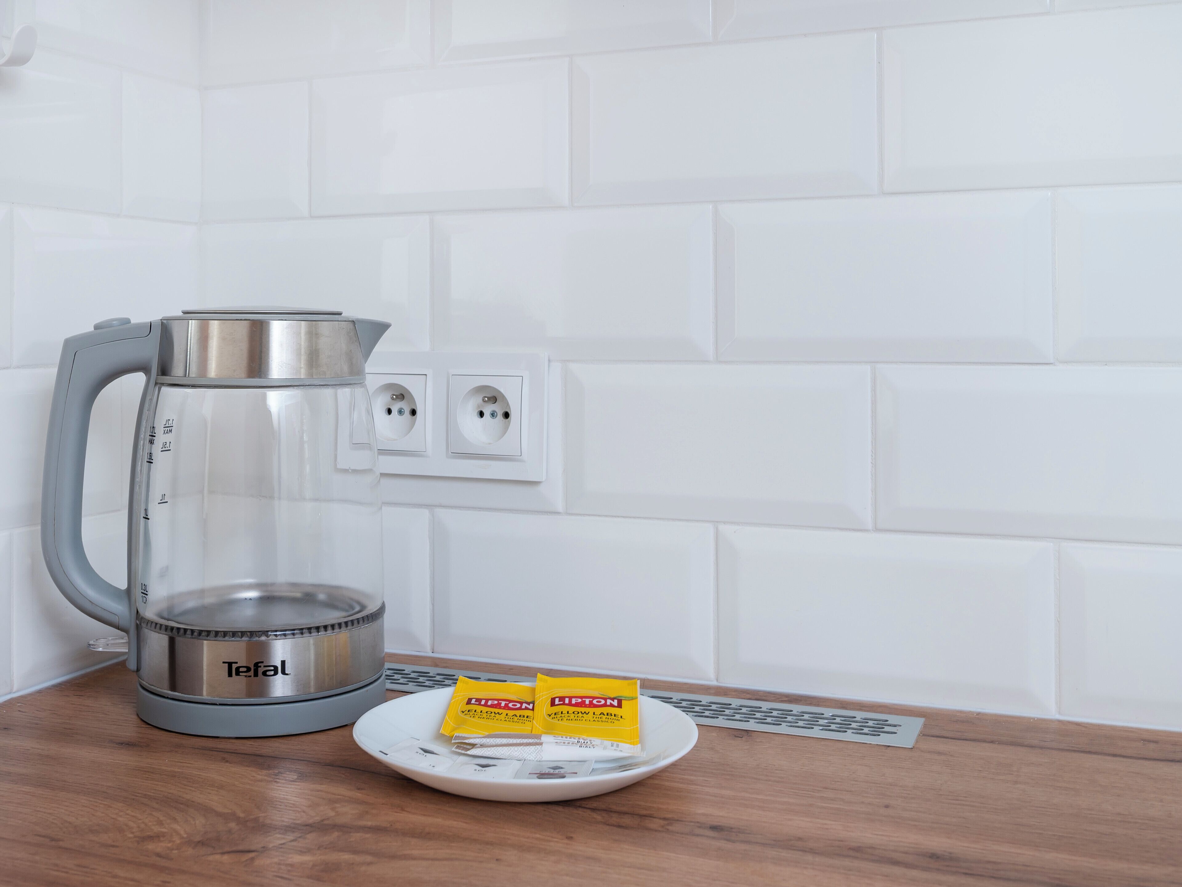 A kitchen with a Tefal electric kettle, a white plate with Lipton tea bags, and a power outlet on the wall.
