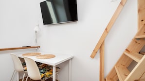 Ein modernes Zimmer mit einem weißen Tisch, zwei Stühlen, einem Flachbildfernseher, einer Lampe und einer Holztreppe.