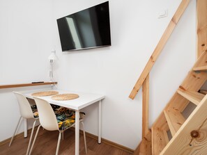 A modern room with a white table, two chairs, a flat-screen TV, a lamp, and a wooden staircase. - Kamienica Rewolucji 23 Mezzanine Studio (Łódź)