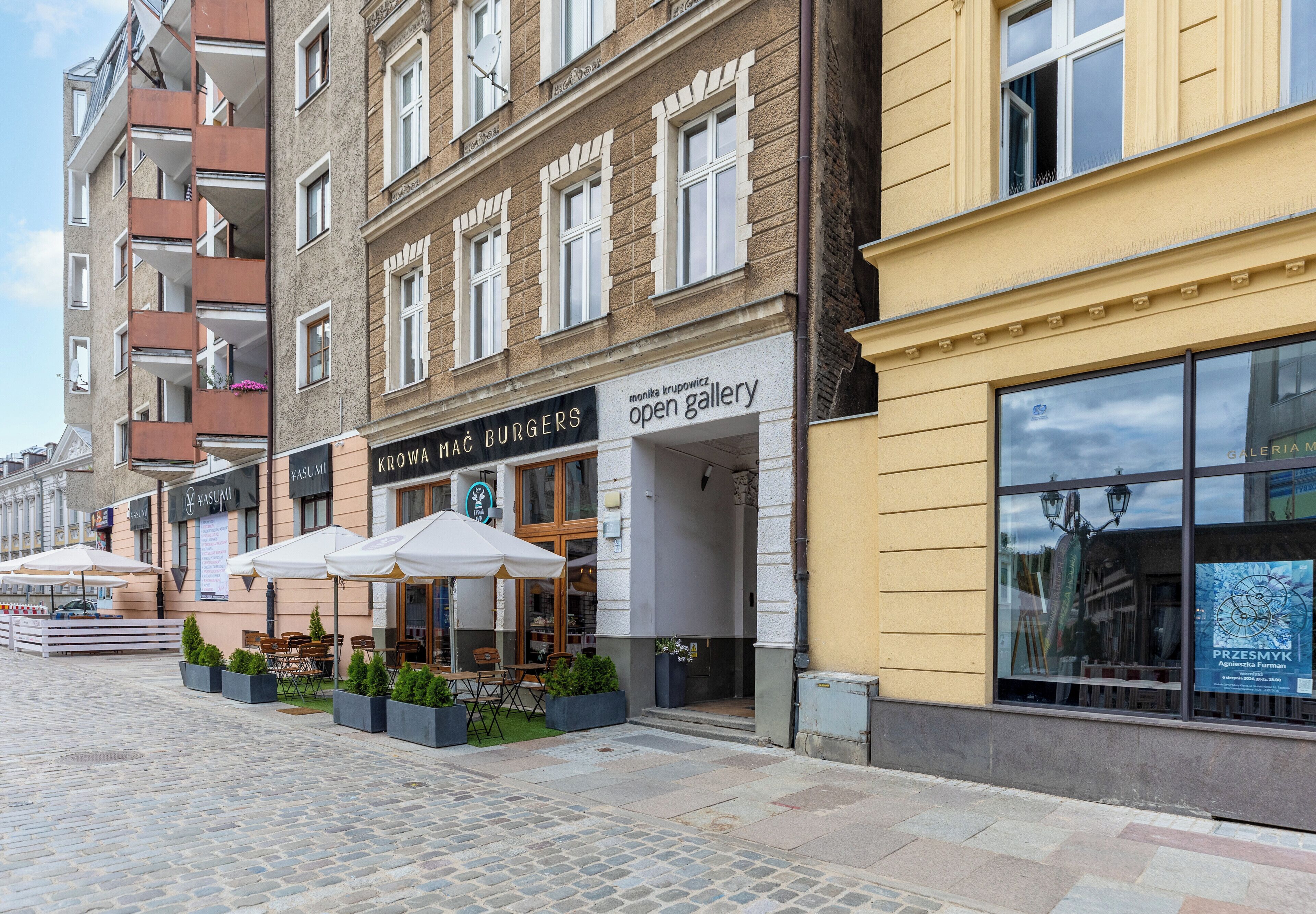 A street with outdoor seating and a variety of shops, including a gallery and a restaurant.