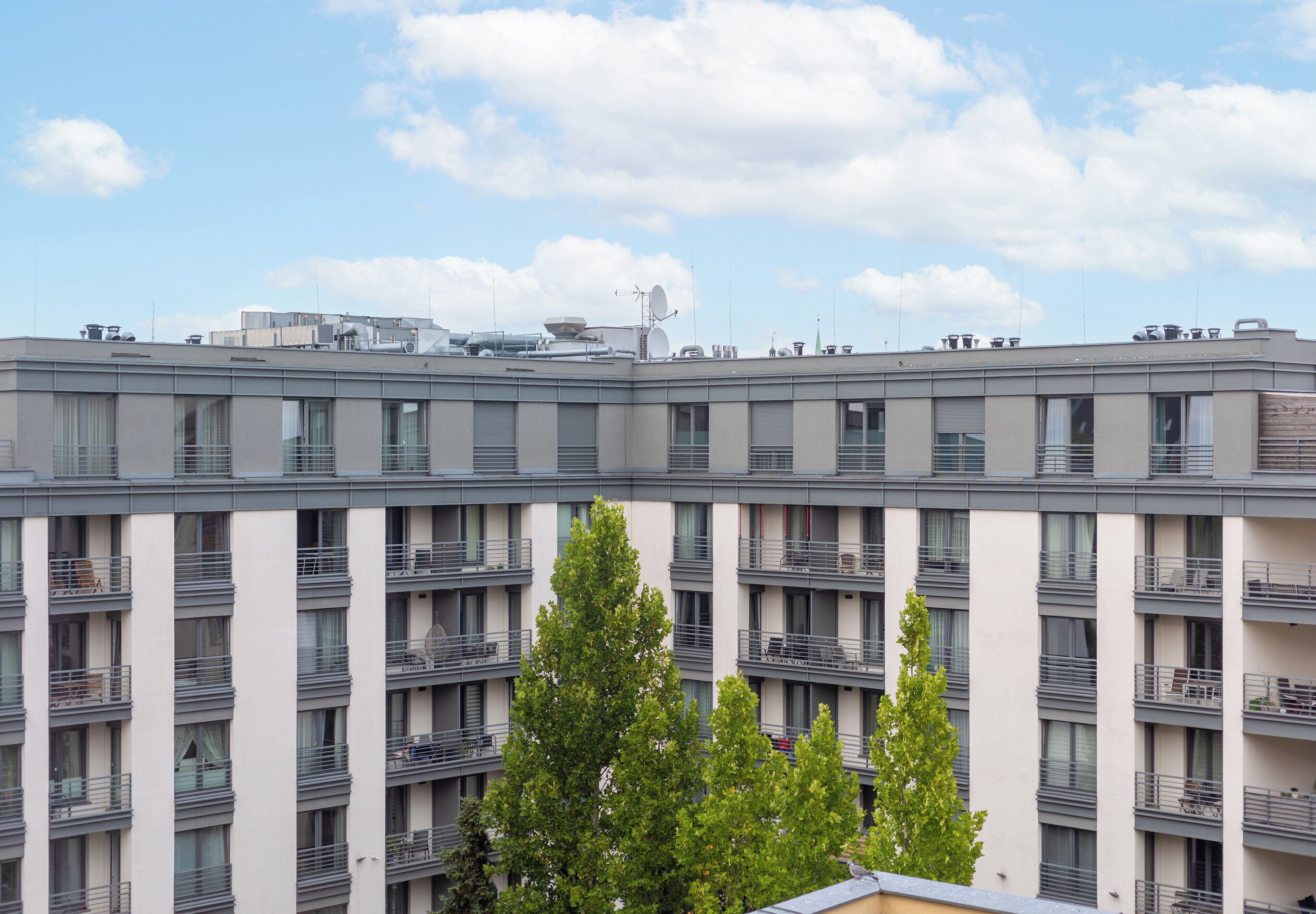 A multi-story building with balconies, a flat roof with various equipment, and a clear sky.