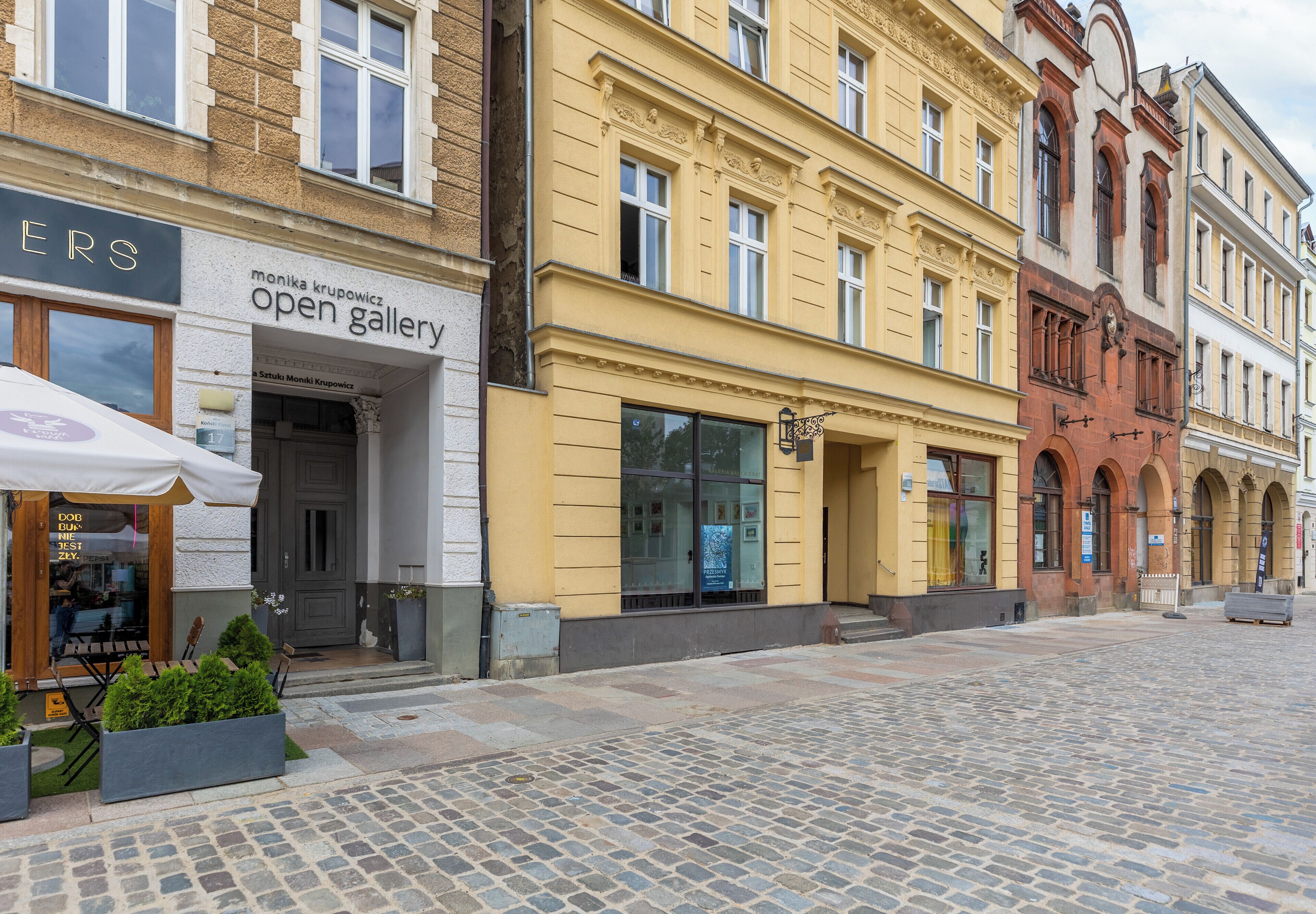 A cobblestone street with a row of buildings, including a gallery and a restaurant.