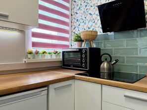 A kitchen with a built-in toaster oven, a kettle, and a window with blinds. - Jelenia Góra Comfort Studio (Jelenia Góra)