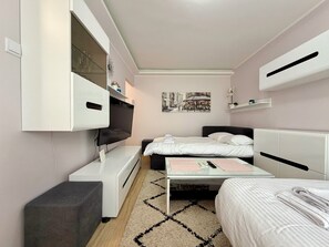 A compact bedroom with a bed, bedside tables, a desk, a TV mounted on the wall, and a small seating area.