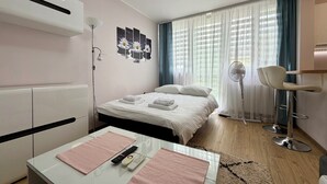Ein modernes Hotelzimmer mit Bett, Nachttisch, Lampe und Blick ins Freie durch transparente Vorhänge.
