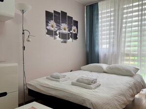 A neatly made bed with white linens and towels, a bedside lamp, and a wall with three framed pictures of daisies. - Jelenia Góra Comfort Studio (Jelenia Góra)