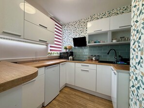 A modern kitchen with white cabinetry, a wooden countertop, a built-in microwave, and a tiled backsplash. - Jelenia Góra Comfort Studio (Jelenia Góra)