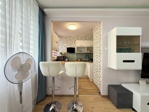 A modern kitchen with a microwave, kettle, and a patterned backsplash. There are two white bar stools and a white cabinet with glass doors. - Jelenia Góra Comfort Studio (Jelenia Góra)