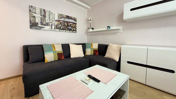Ein modernes Wohnzimmer mit einer Couch, einem Glastisch, einer Fernbedienung und einer Wand-Klimaanlage.