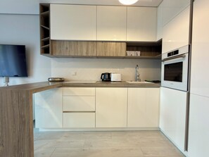 A modern kitchen with white cabinets, a Bosch oven, a coffee maker, and a flat-screen TV mounted on the wall. - Kępa Mieszczańska Spacious Apartment (Wrocław)