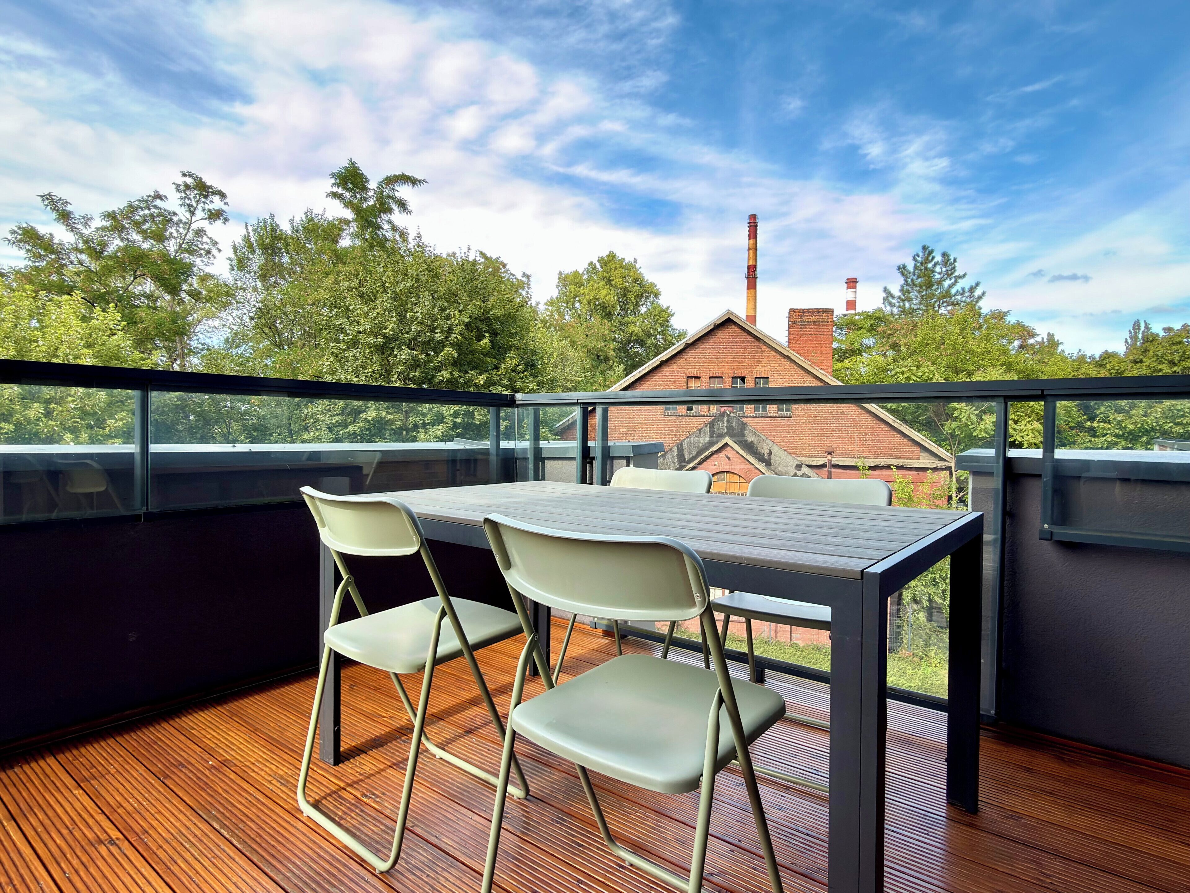 Een balkon met een tafel en stoelen, met uitzicht op een gebouw met schoorstenen.