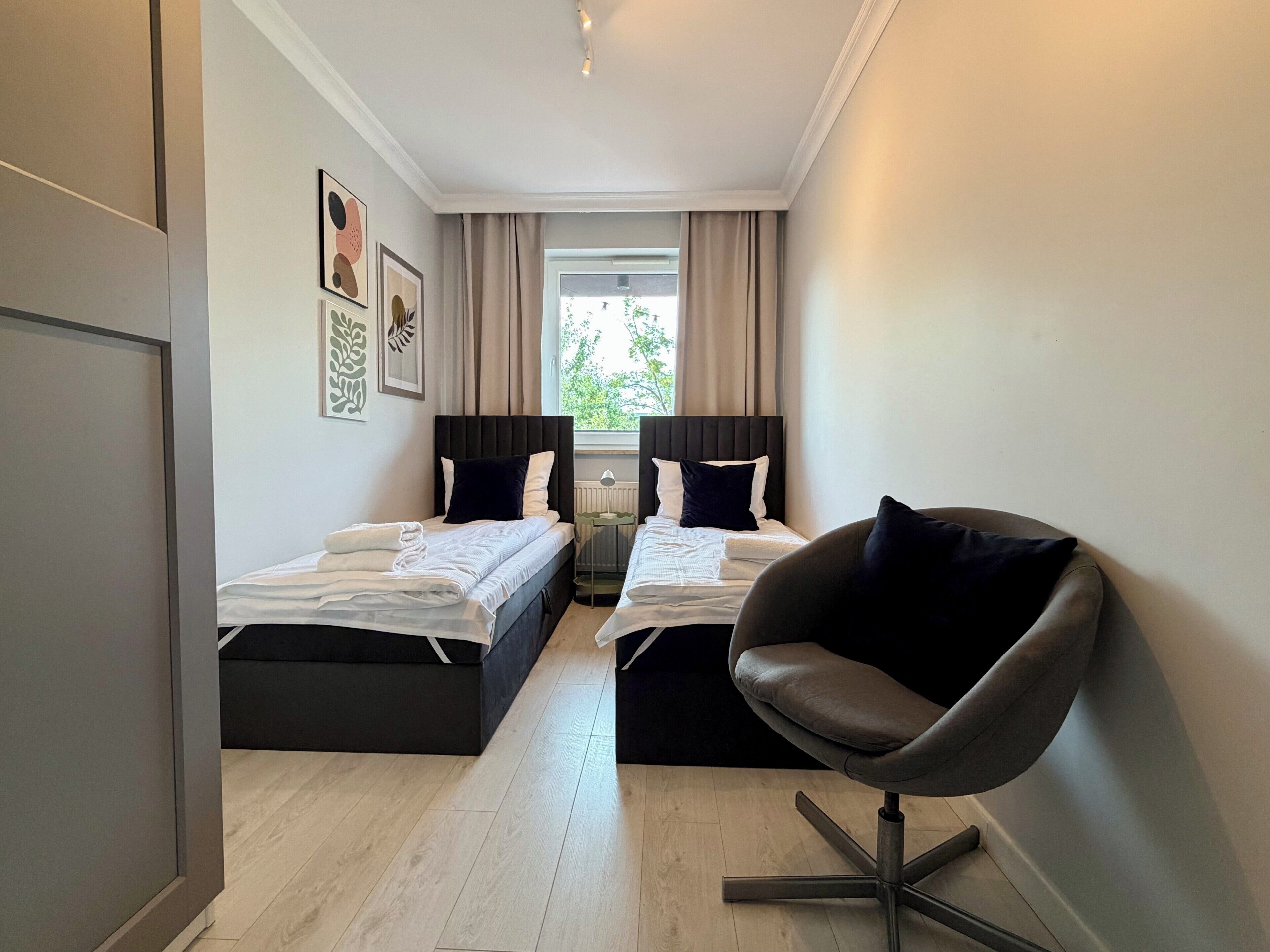 A hotel room with two beds, a modern chair, and a window with curtains.