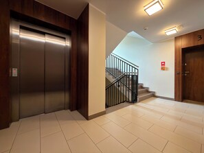Un ascensor moderno, una escalera con barandilla y una puerta con número.